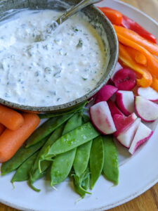 A bowl of easy veggie dip on a plate with raw veggies.
