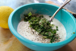 Making parmesan herb veggie dip, adding in the fresh herbs in a blue bowl.