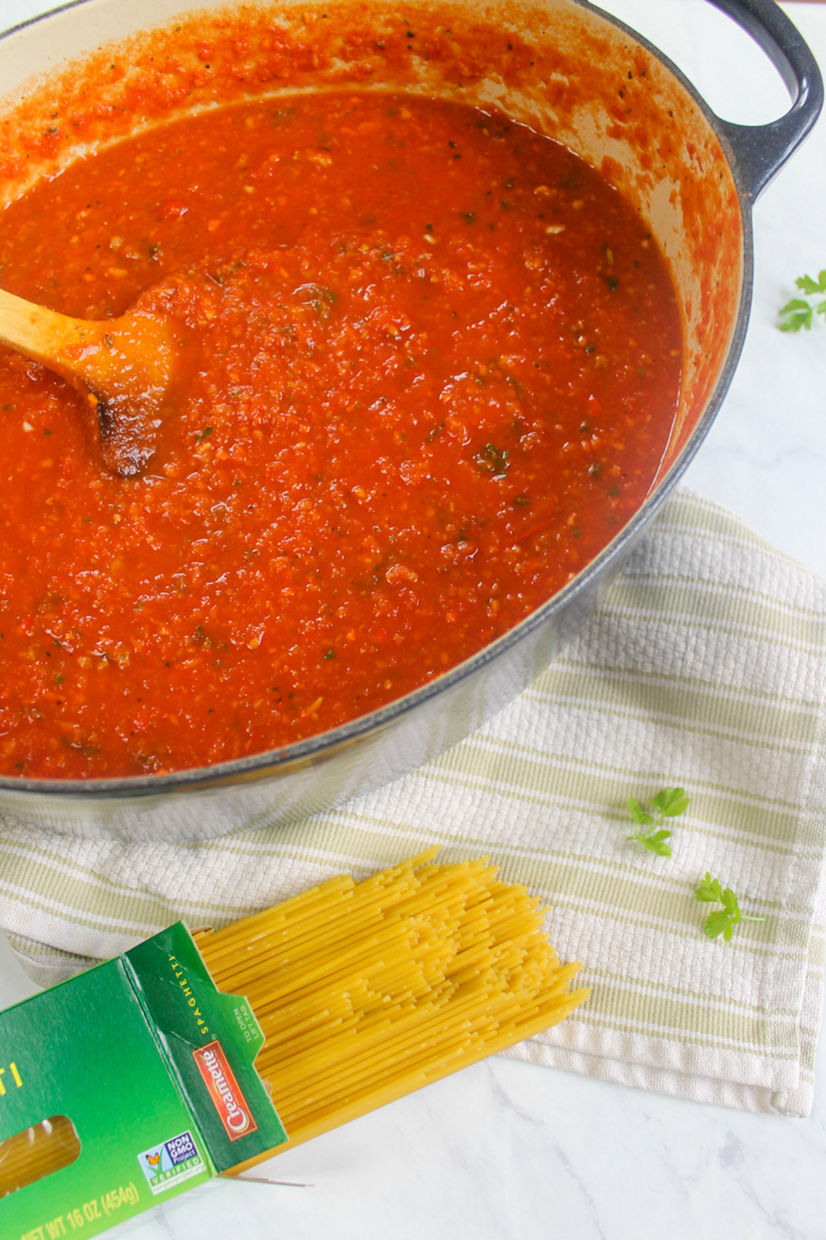 A large pot of red marinara Italian sausage bolognese sauce next to a box of pasta.