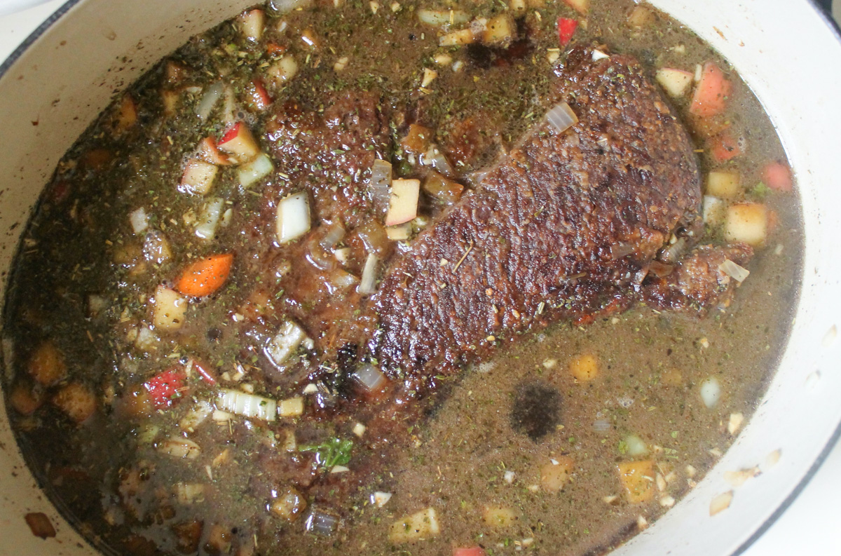 Beef roast in a dutch oven covered in beef stock, ready to braise.