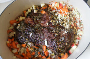The seared beef roast with onion, carrot, apple, garlic and seasonings added.