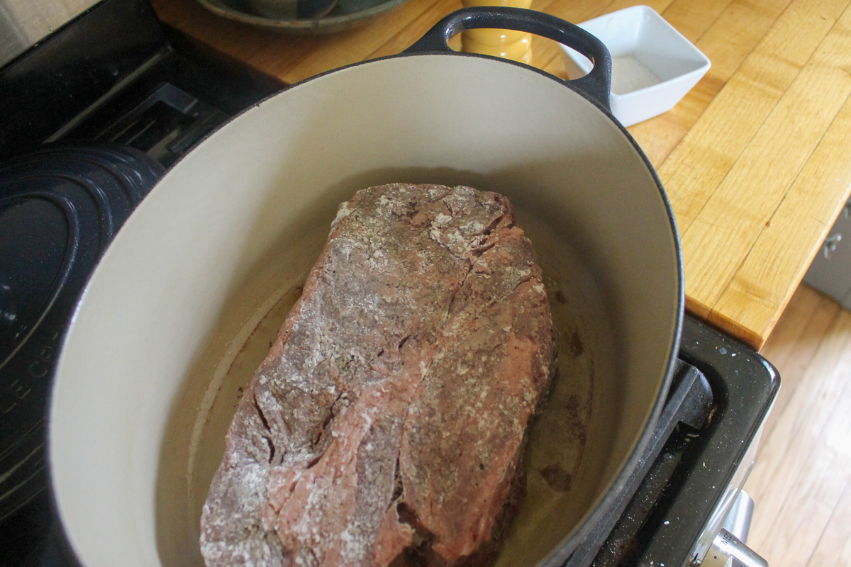 Searing the first side of the beef roast, the raw side exposed and coated with flour.