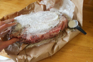 Seasoning the beef roast with salt and pepper and coating it with flour.