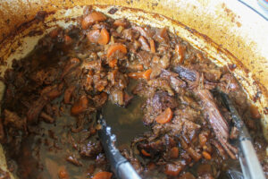 The finished pot of cooked beef roast, tender and shredded with tongs.
