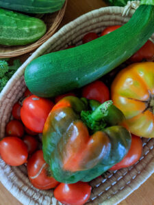 Garden vegetables like bell pepper, zucchini, and tomato in a basket, ready to be chopped and grilled.