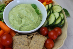A white bowl of whipped avocado dip surrounded by raw veggie to dip.