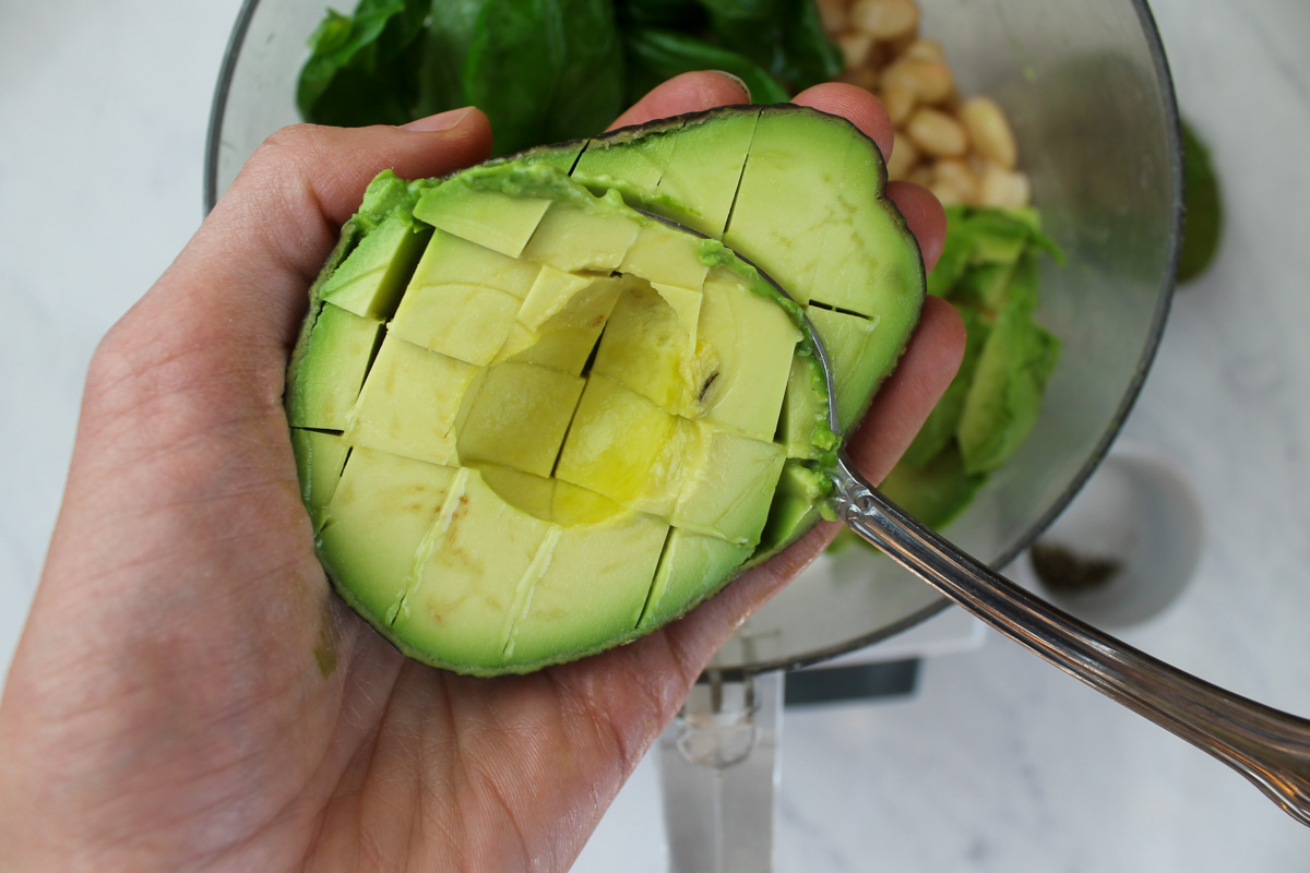 A hand holding a half avocado showing how to slice in a grid and spoon out.