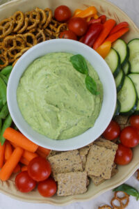 A platter of avocado basil dip surrounded by veggies.