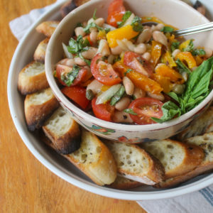 Bowl of white bean bruschetta surrounded by a plate of toasted crostini.