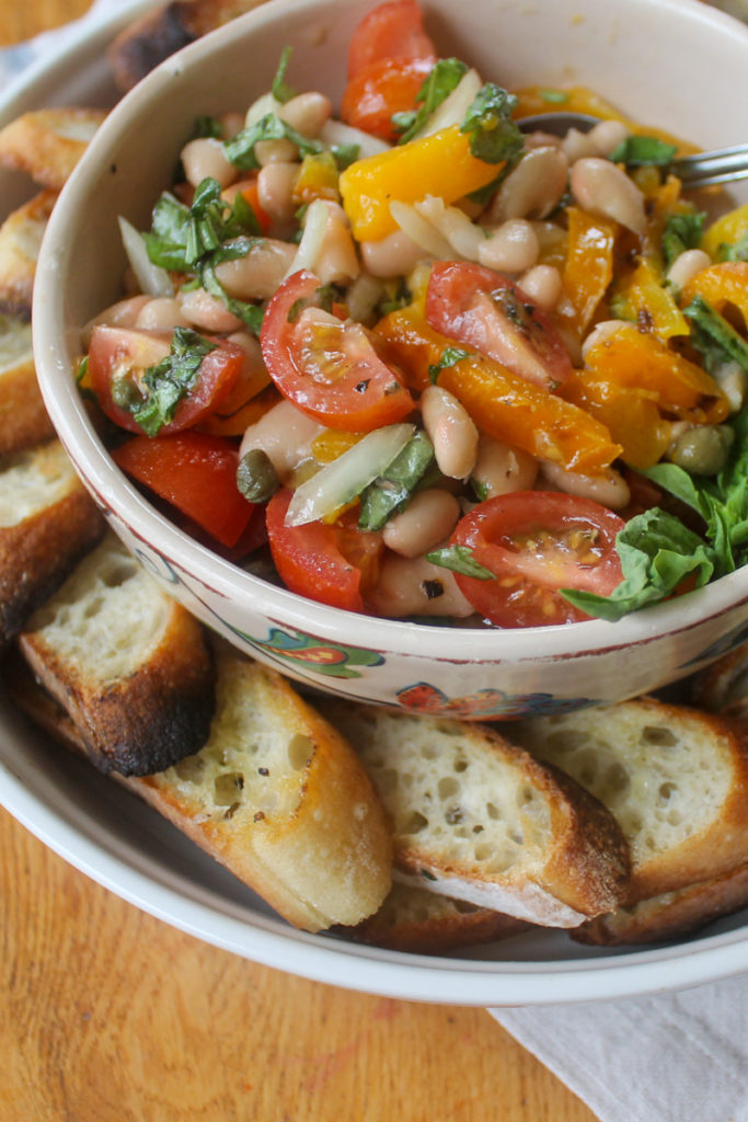 Bowl of white bean bruschetta with Parmesan and toasted baguette slices.