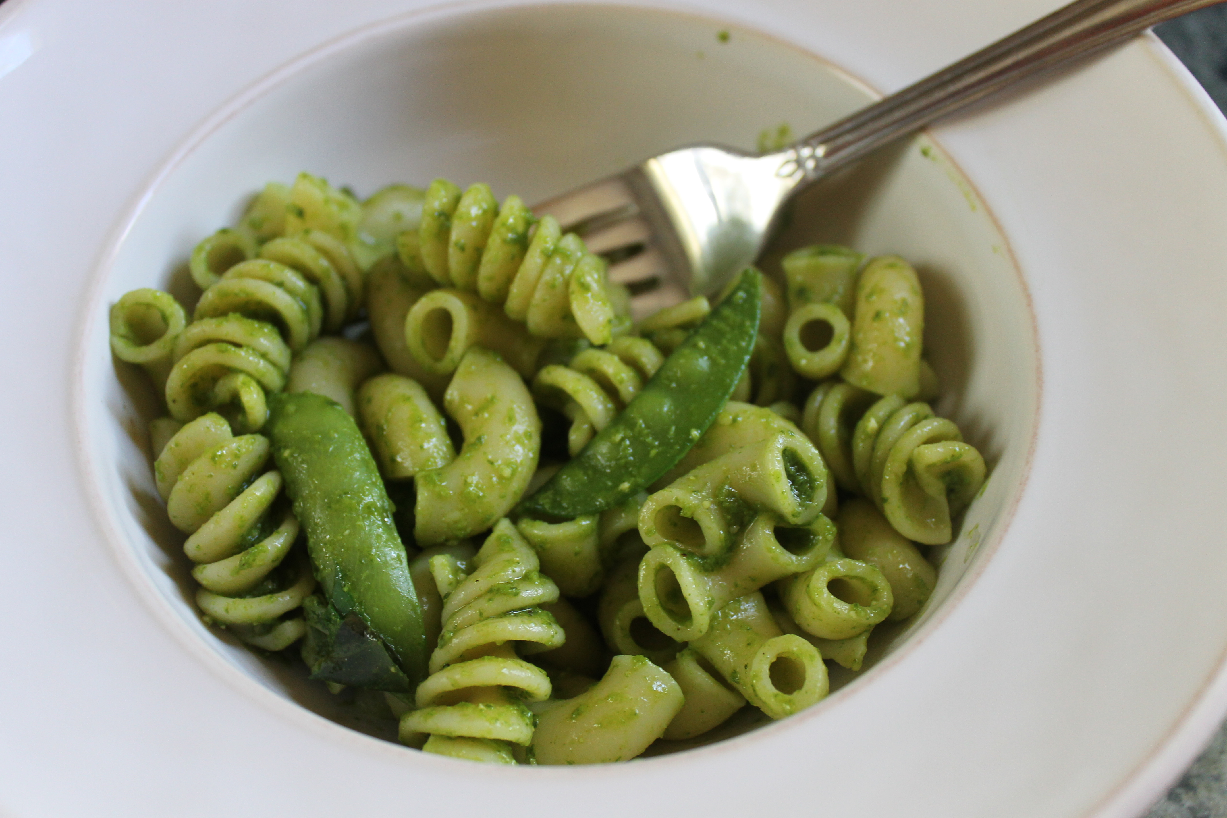 A bowl of pasta and pea pods with pesto sauce.