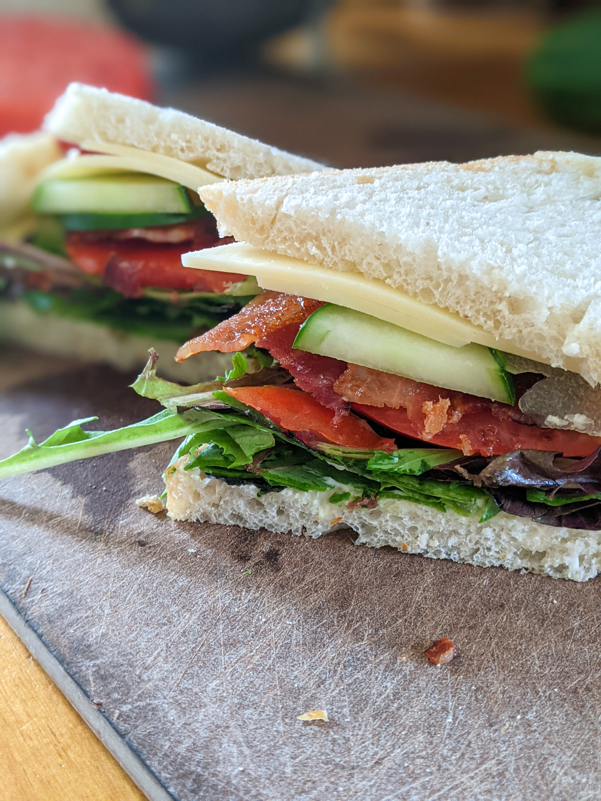 A BLT sandwich on white bread with cucumber and avocado.