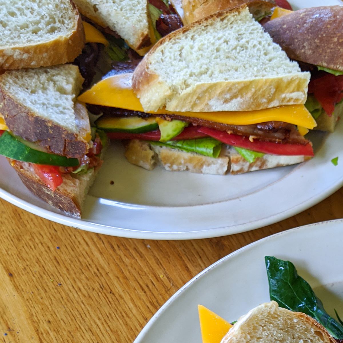 A plate of BLT's cut in half with cheese and avocado.