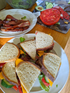 A plate of BLT's with bacon and sliced tomato on a cutting board.