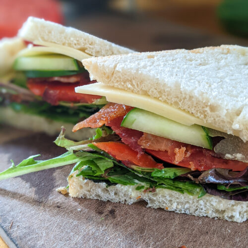 A BLT with cheese and avocado, sliced in half.