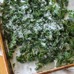 A sheet pan of baked kale chips topped with Parmesan cheese.