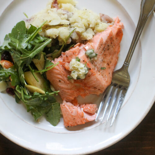 A plate of salmon with honey butter, potatoes and salad.