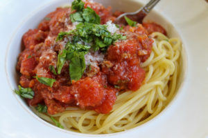 Homemade spaghetti meat sauce over pasta with chopped basil.