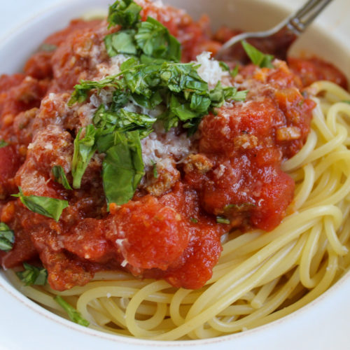 Homemade spaghetti meat sauce over pasta with chopped basil.