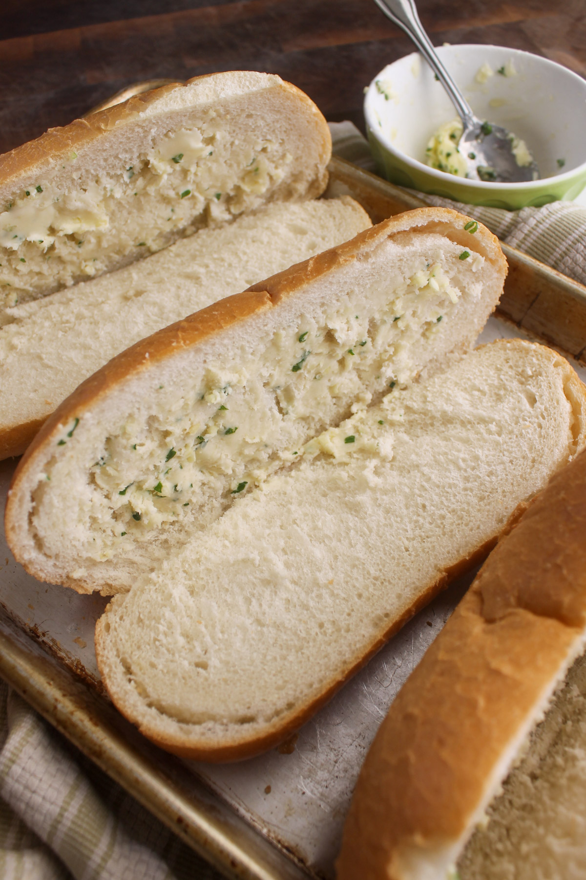 Spreading garlic honey butter on sliced open hoagie buns ready to bake on a sheet pan.