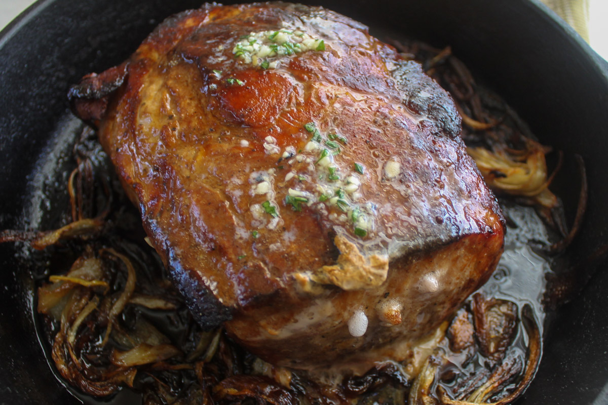 The finished pork roast surrounded by cooked onions and topped with the melting garlic honey butter.