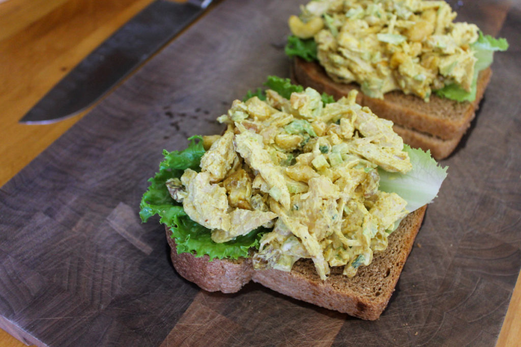 Curry Chicken Salad being prepared on toasted sandwich bread with lettuce.