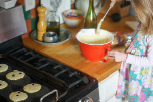 Child helping make old fashioned buttermilk pancake recipe on griddle.