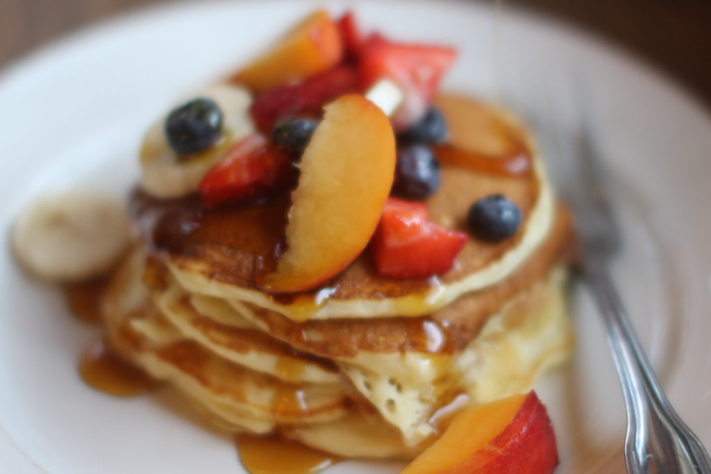 Plate of Mom's Buttermilk Pancakes topped with fruit and maple syrup.