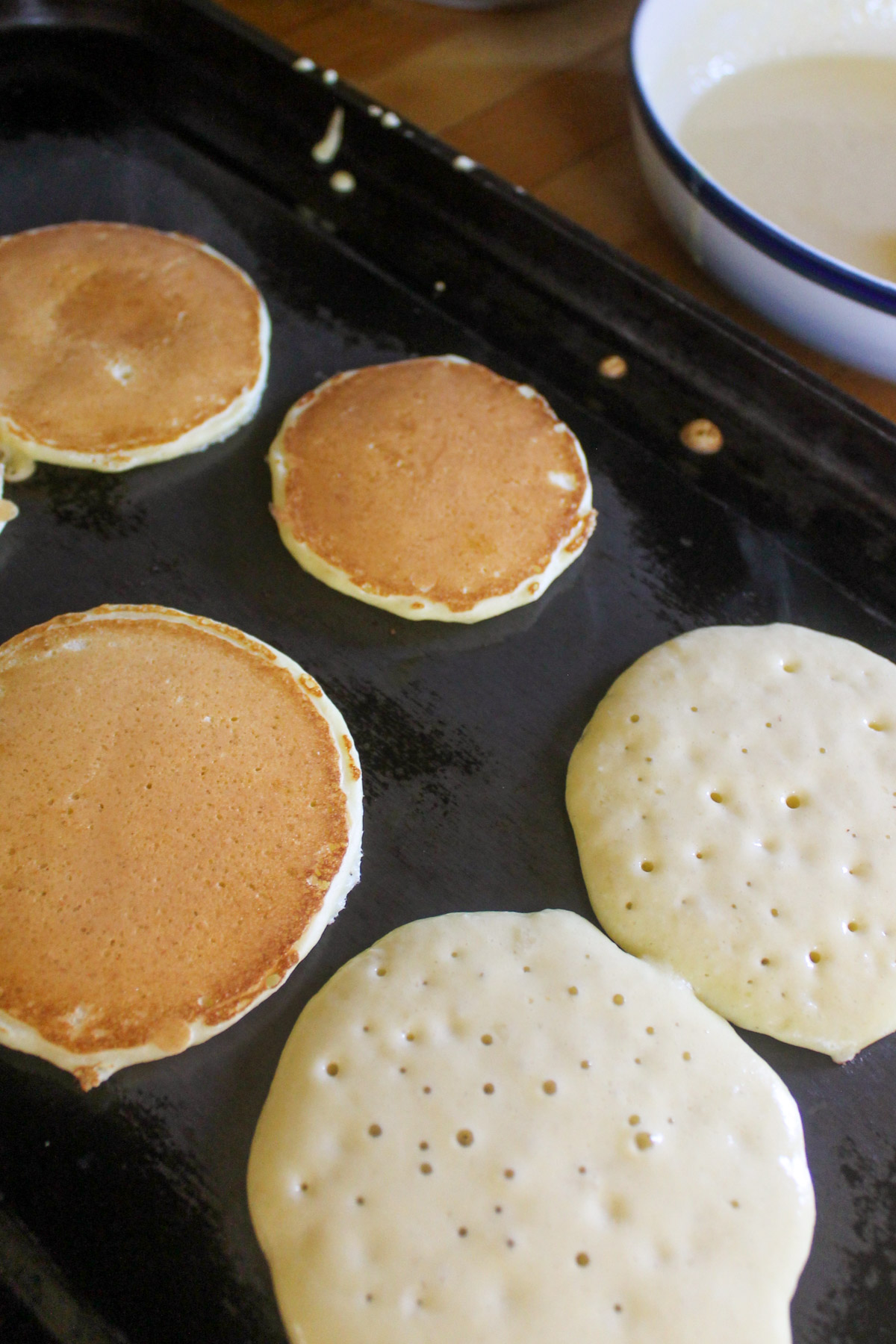 Pancakes on a griddle, some flipped and some not flipped.