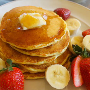 A stack of protein buttermilk pancakes with a pat of butter and maple syrup.