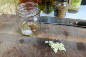 Minced garlic on a cutting board and a jar of vinaigrette ingredients.