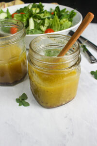 Mason jar salad dressing in front of a white bowl of lettuce salad.