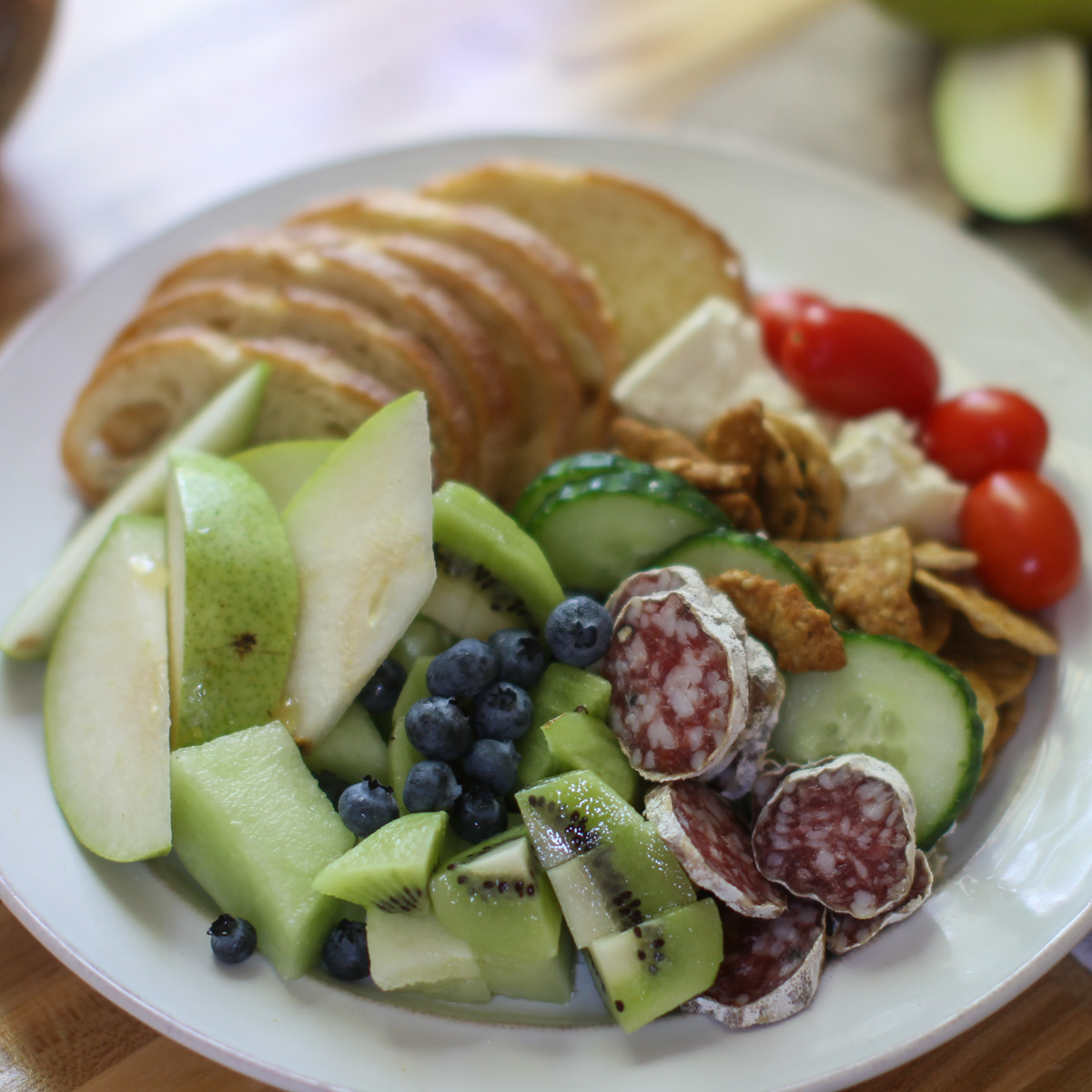 A healthy charcuterie lunch with fruits and veggies, salami and sliced baguette.