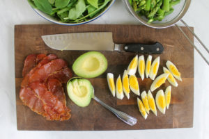 Prepared ingredients on a cutting board, chopped hard boiled egg, avocado, crispy prosciutto.
