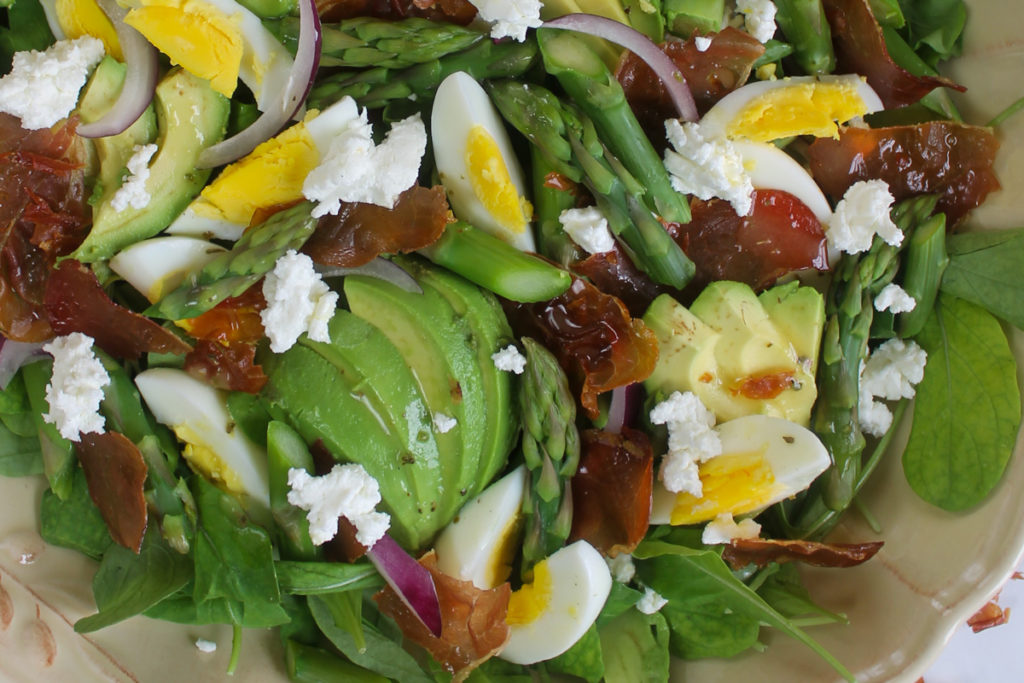 Close up of asparagus prosciutto salad with hard boiled egg and goat cheese.