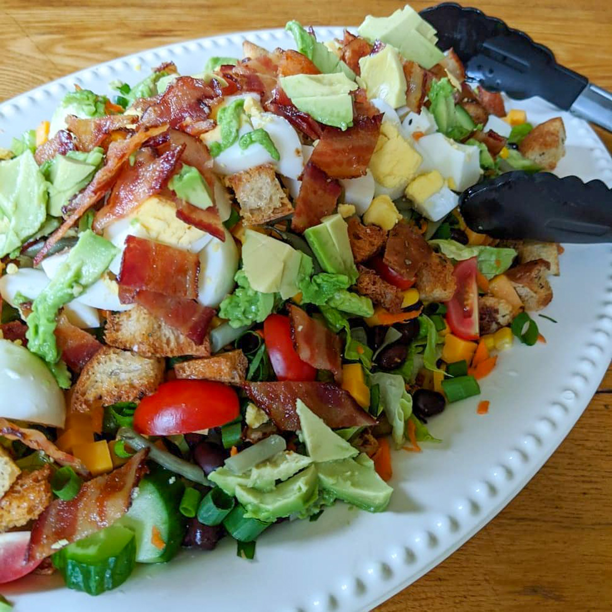 A green salad with roasted potatoes on a white platter for dinner.