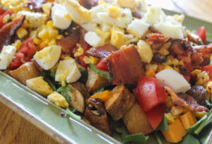 A colorful dinner salad with lots of veggies, bacon, egg and corn.