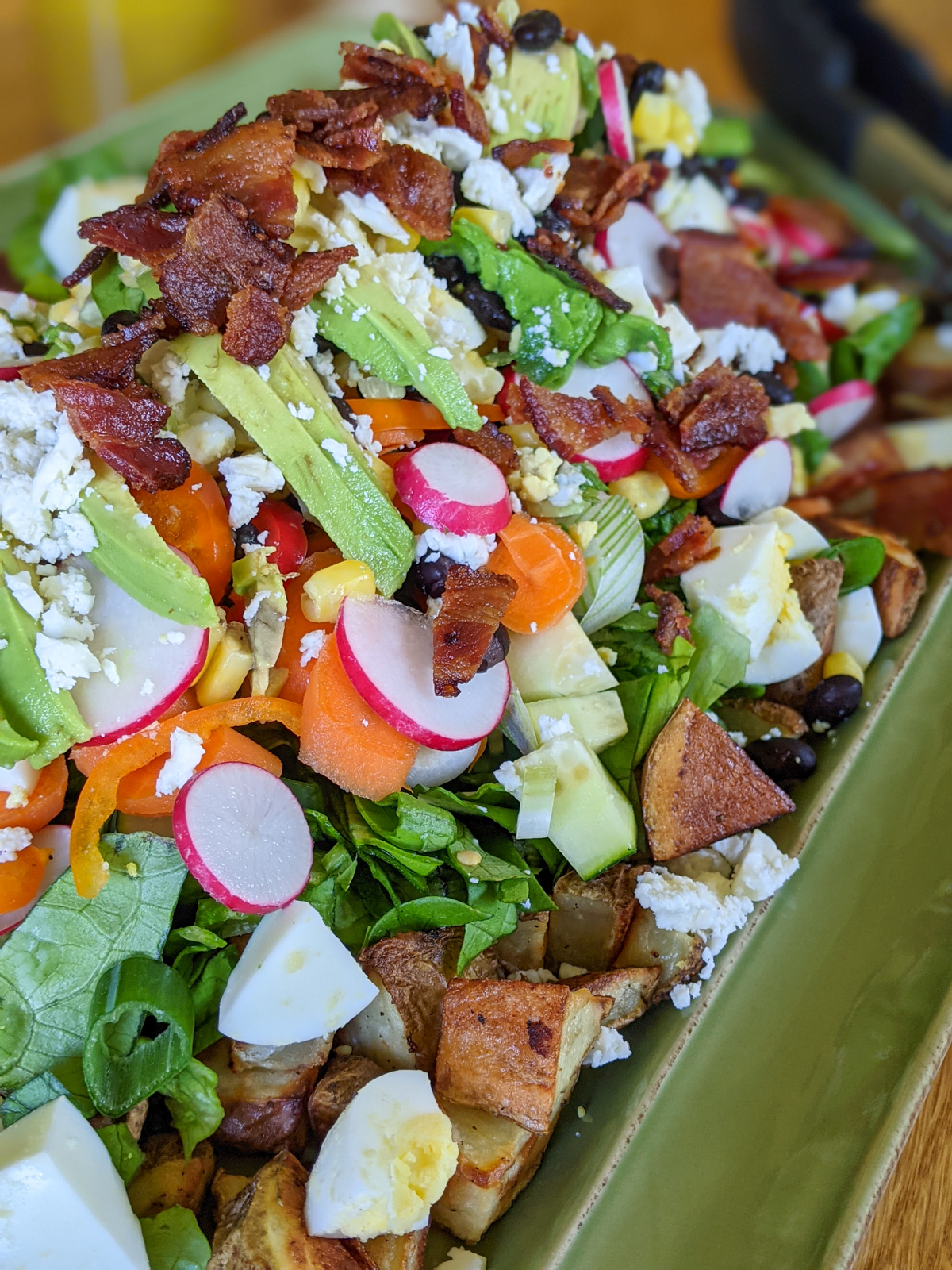A raw and roasted dinner salad with potatoes, bacon, radishes, greens and crumbled cheese.