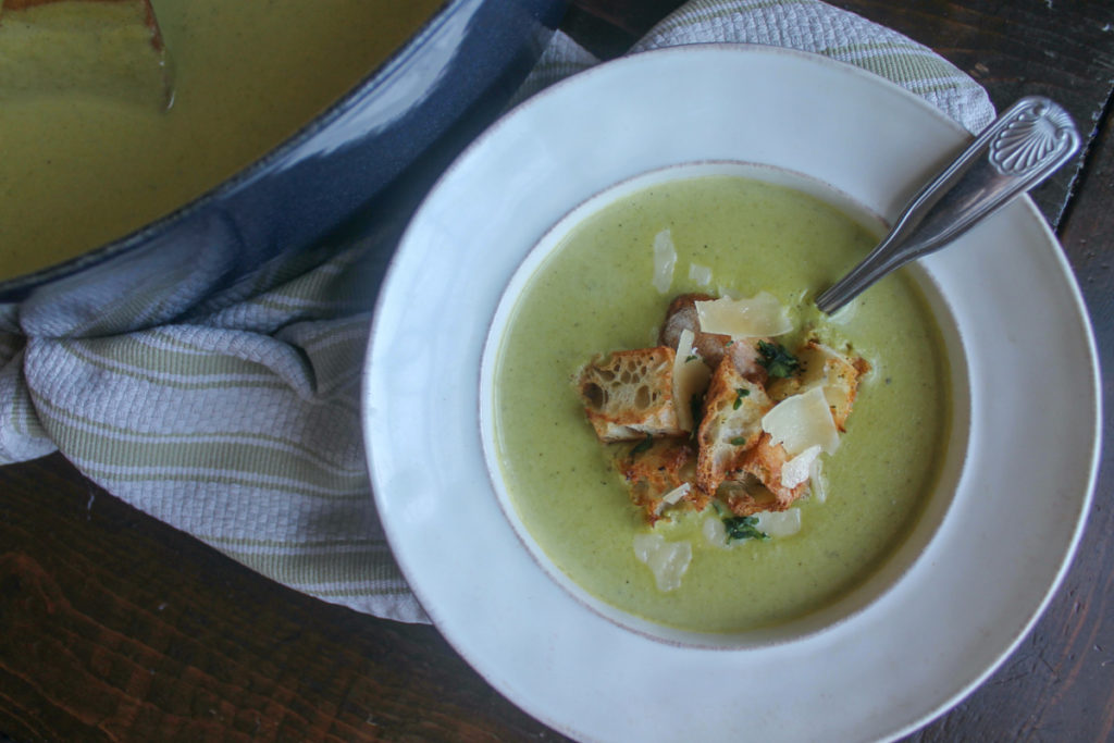Bowl of asparagus soup next to the pot of soup.