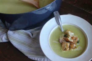Large pot of asparagus soup next to a bowl of soup with croutons.