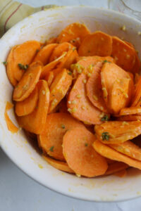 Mixing the sweet potato slices in a bowl with the garlic honey butter.