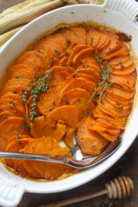 A casserole pan of roasted sweet potato rounds with fresh thyme.