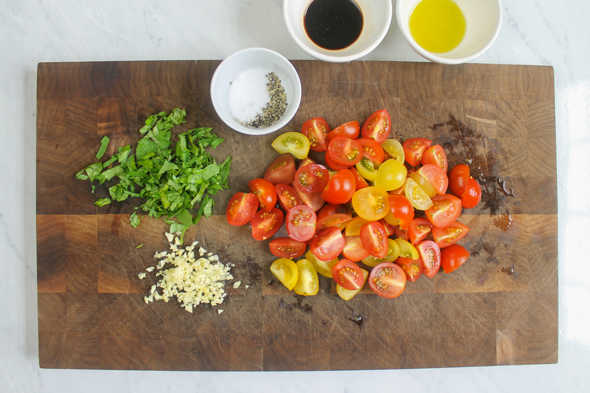 Cherry tomatoes, basil and garlic, chopped and prepped on a cutting board.