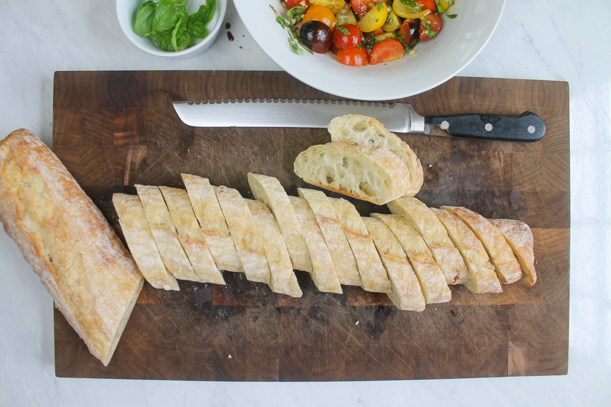 Baguette being sliced at an angle to bake for bruschetta.