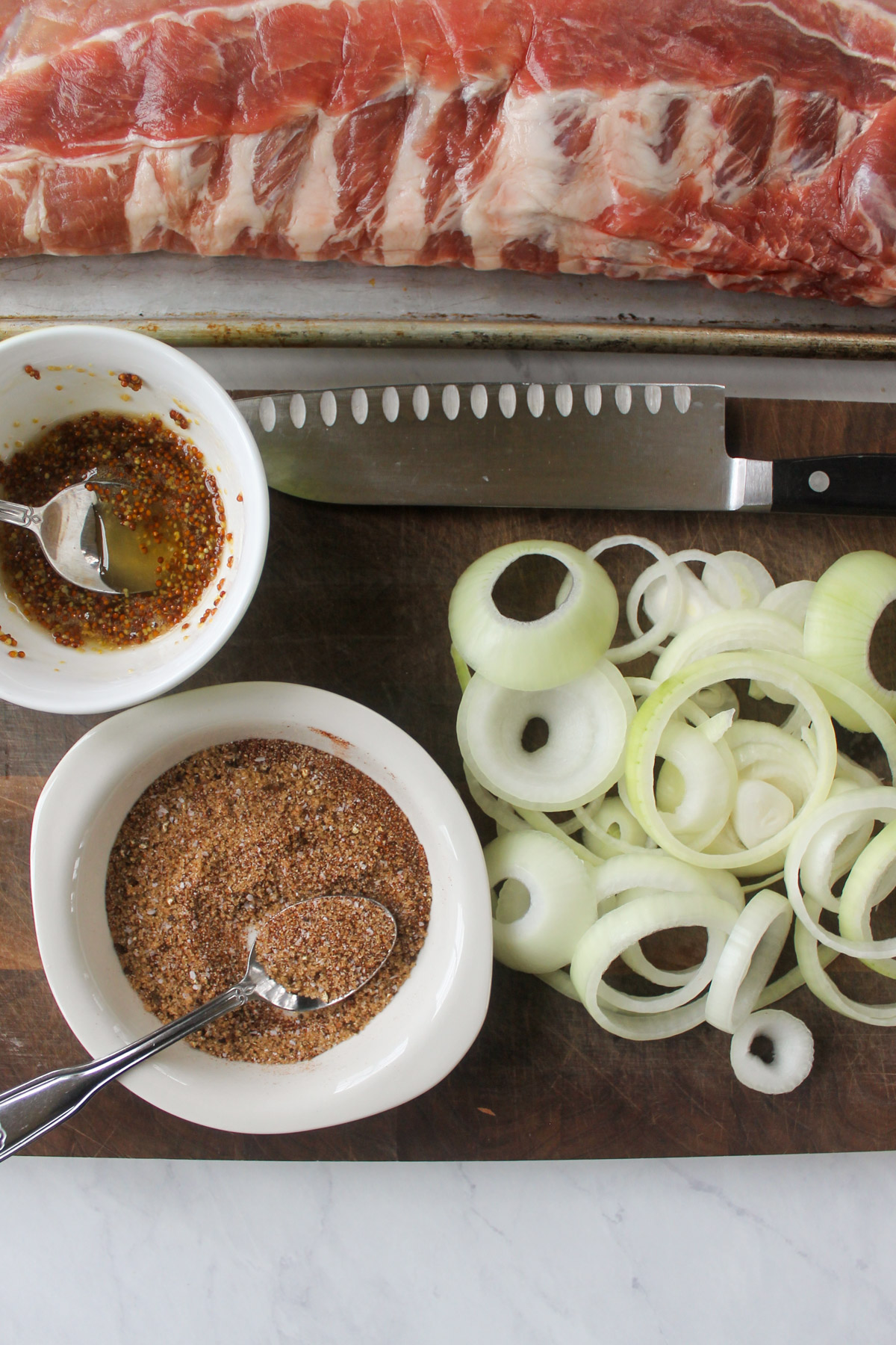 A bowl of dry rub on a cutting board with onions sliced into rings and a bowl of honey mustard.