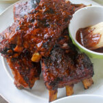 BBQ ribs on a plate with a bowl of extra sauce.