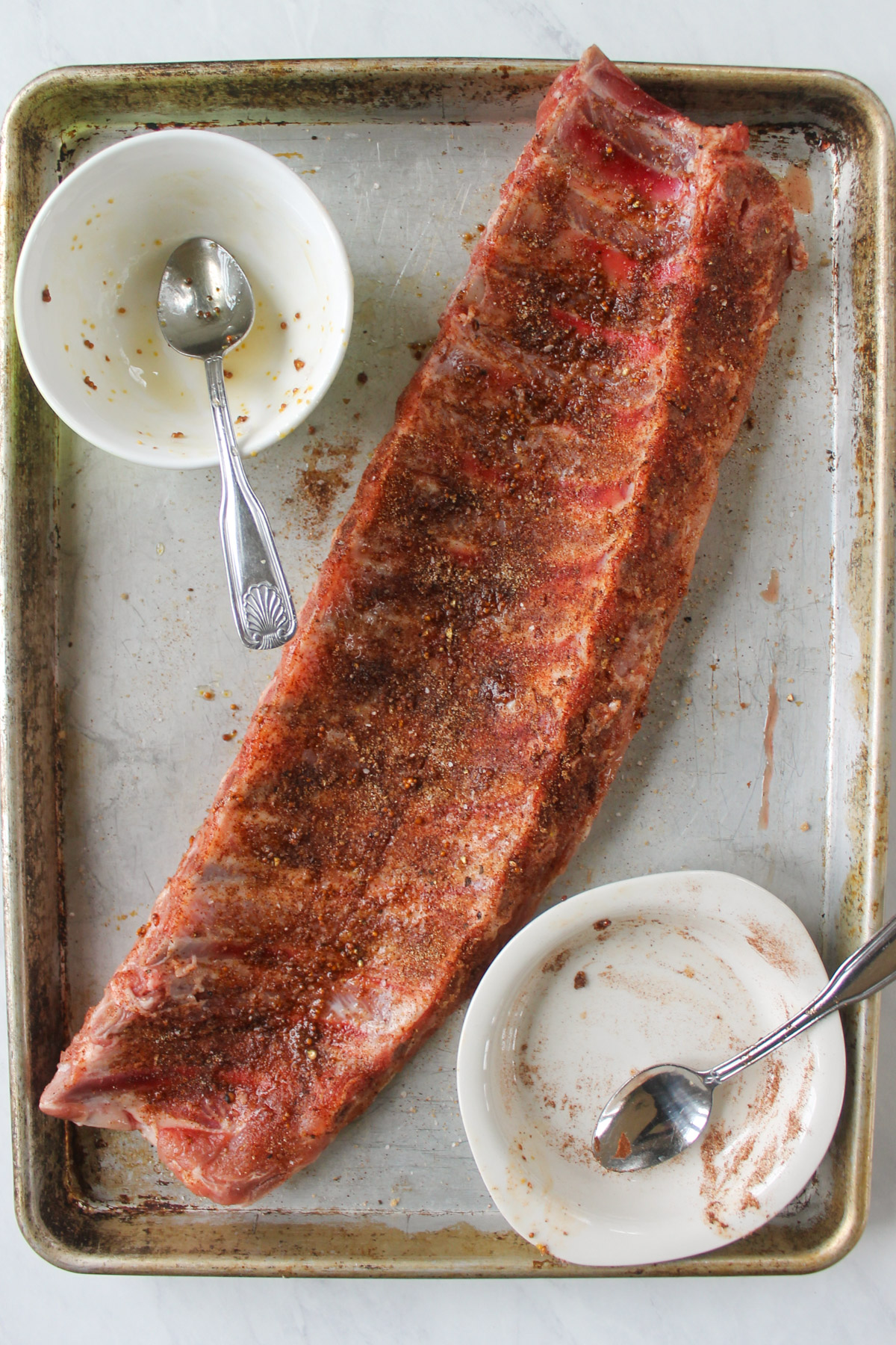 A rack of pork ribs on a sheet pan that have been coated in dry rub seasoning.