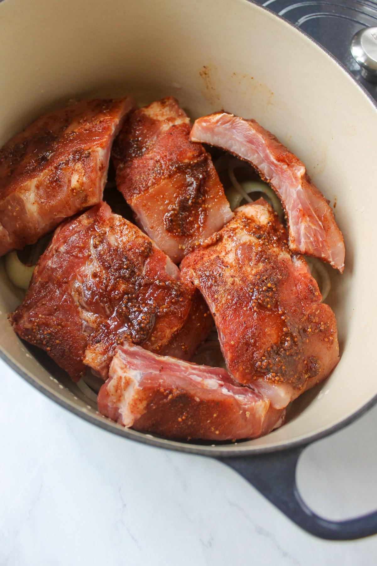 The rack of ribs with the dry rub, cut into large pieces and arranged in a Dutch oven, ready to bake.
