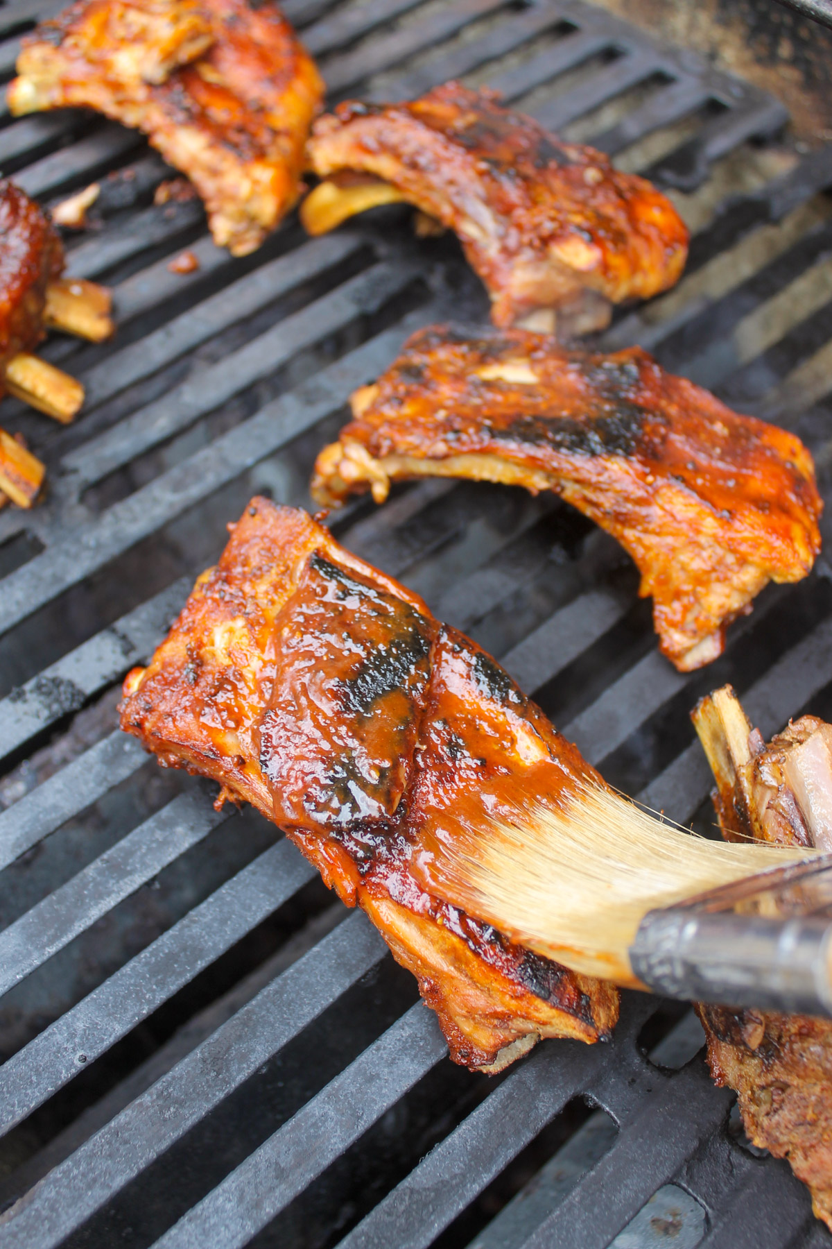 Ribs on the grill being brushed with barbecue sauce.