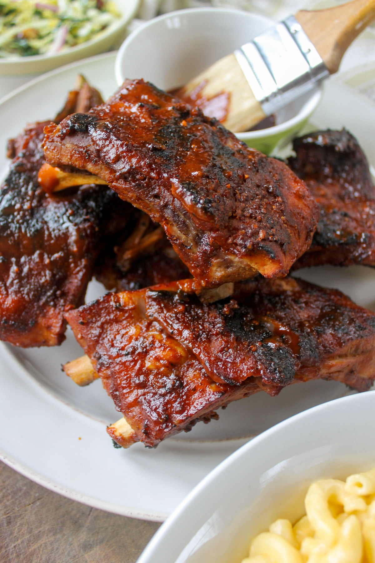 A plate of baby back ribs grilled with barbecue sauce with side dishes around it.